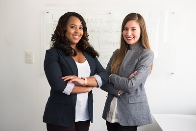Two young women in professional attire standing near a whiteboard