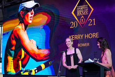 Kerry Hore wearing a black dress. There is a large rower image of her in the background. 